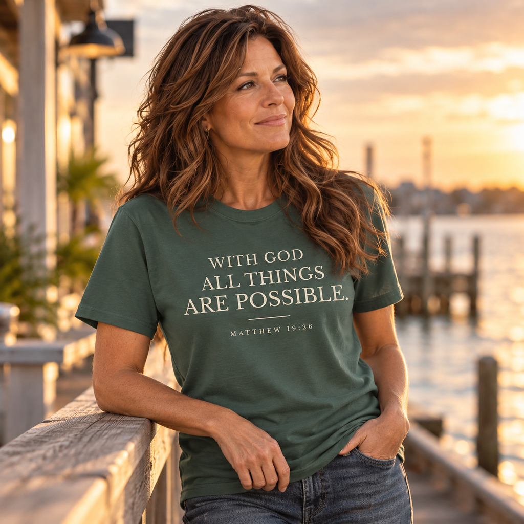 Woman wearing a green Matthew 19:26 Scripture T-shirt while leaning on a waterfront railing.