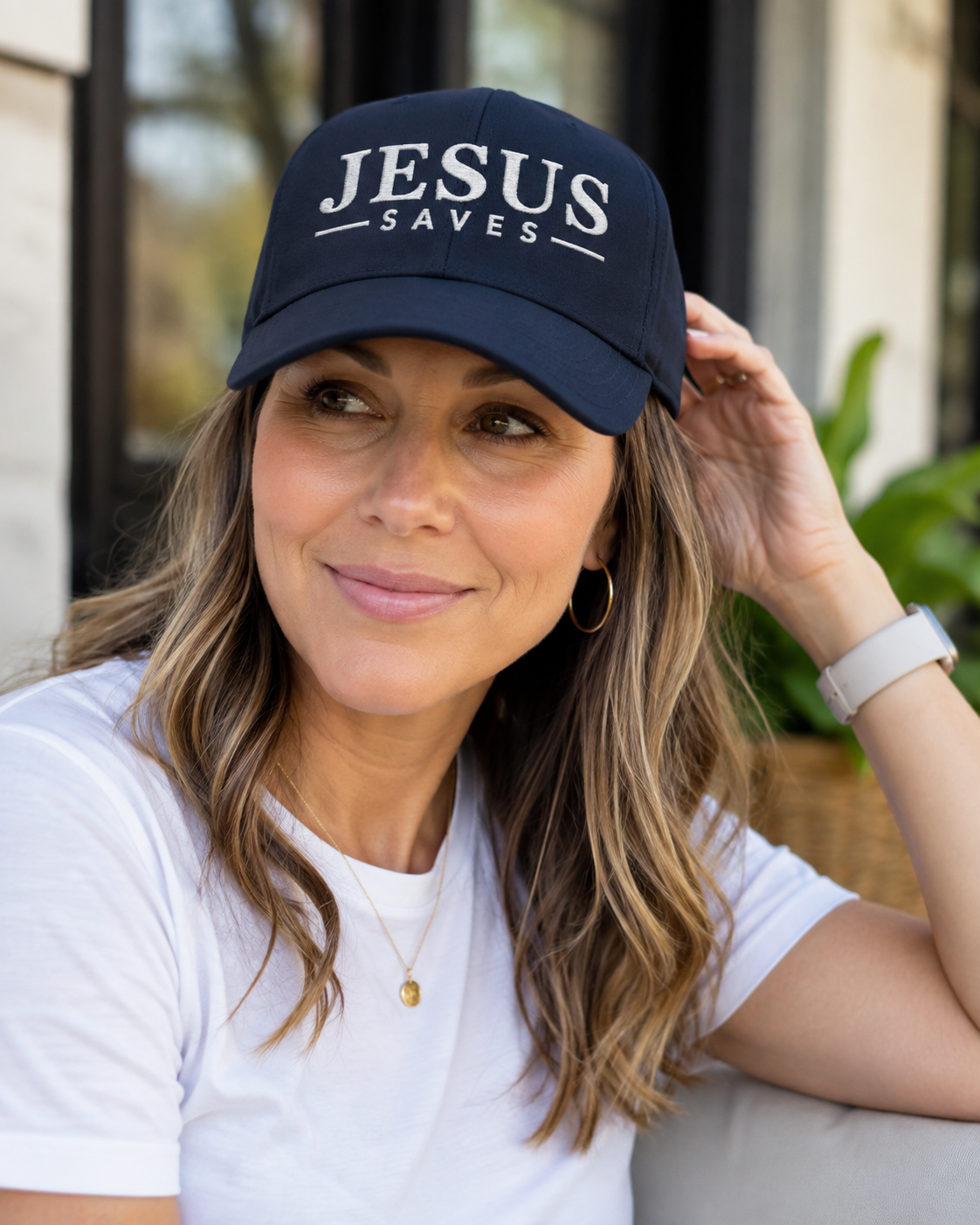 A woman wearing a navy blue baseball cap with 'JESUS SAVES' embroidered in white on the front, paired with a white t-shirt.