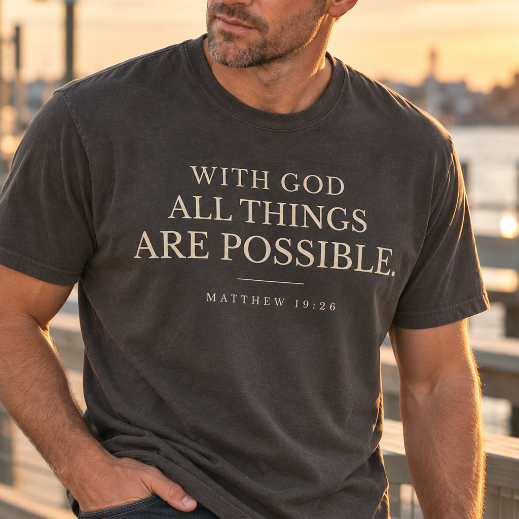 Close-up of a pepper colored Christian T-shirt featuring With God All Things Are Possible typography and Matthew 19:26.
