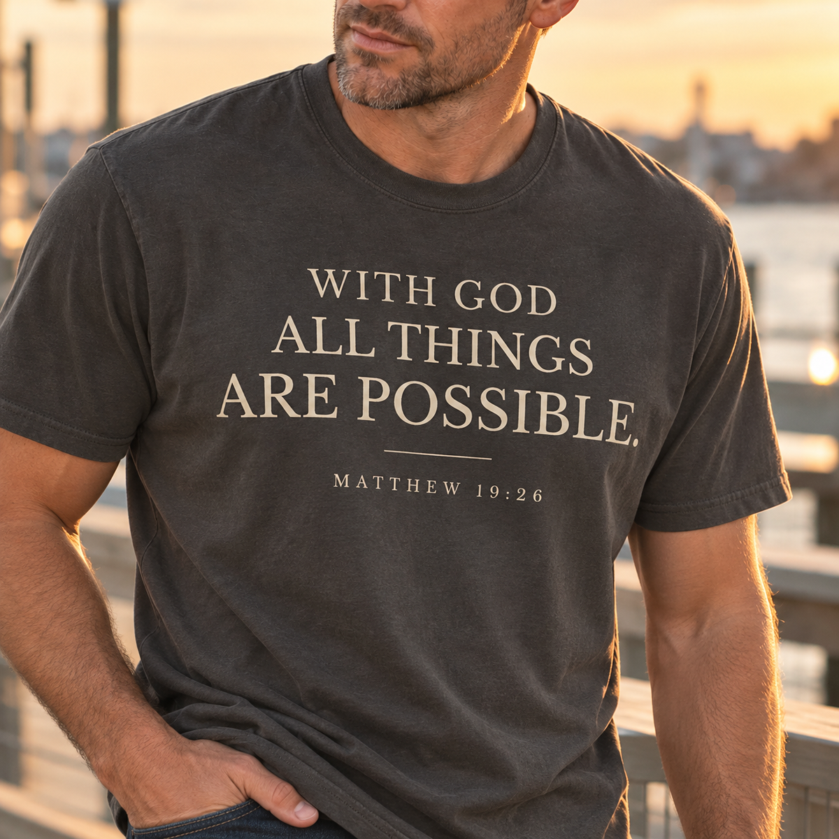 Close-up of a pepper colored Christian T-shirt featuring With God All Things Are Possible typography and Matthew 19:26.