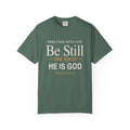 Light green Christian T-shirt reading “When Fear Gets Loud, Be Still and Know He Is God” with Psalm 46:10 on a plain white background.