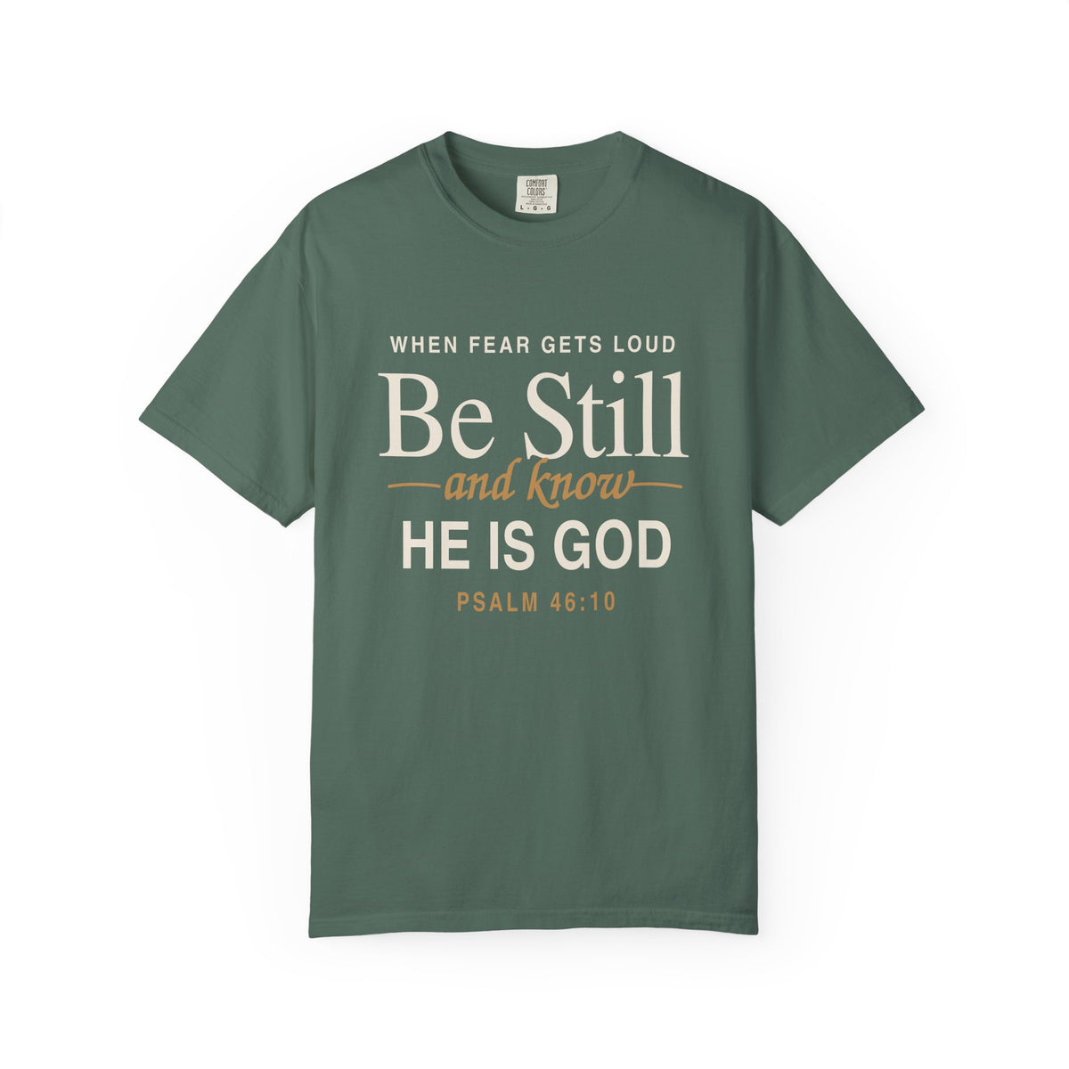 Light green Christian T-shirt reading “When Fear Gets Loud, Be Still and Know He Is God” with Psalm 46:10 on a plain white background.