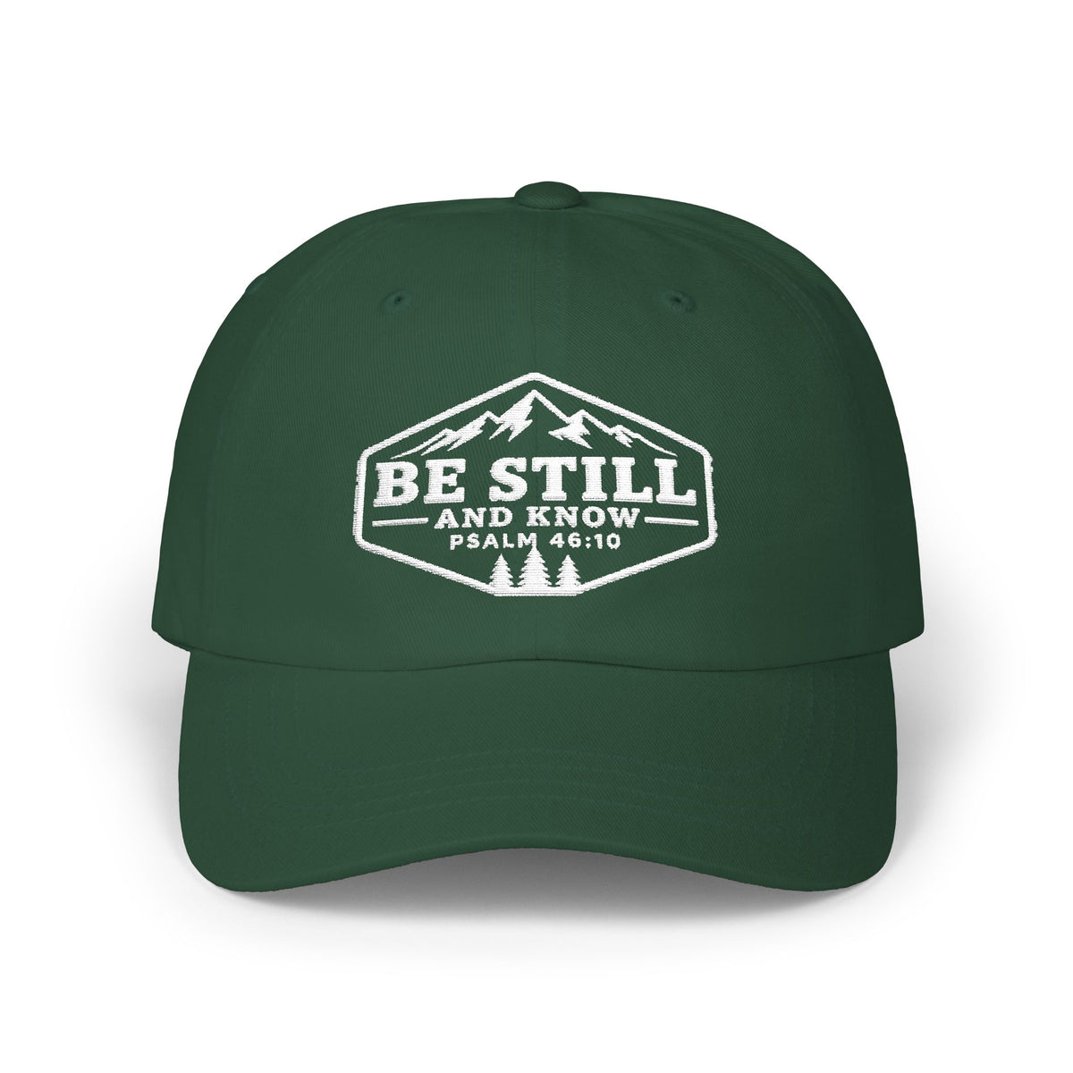 A dark green baseball cap with a white embroidered graphic on the front featuring mountains, pine trees, and the text 'BE STILL AND KNOW PSALM 46:10'.