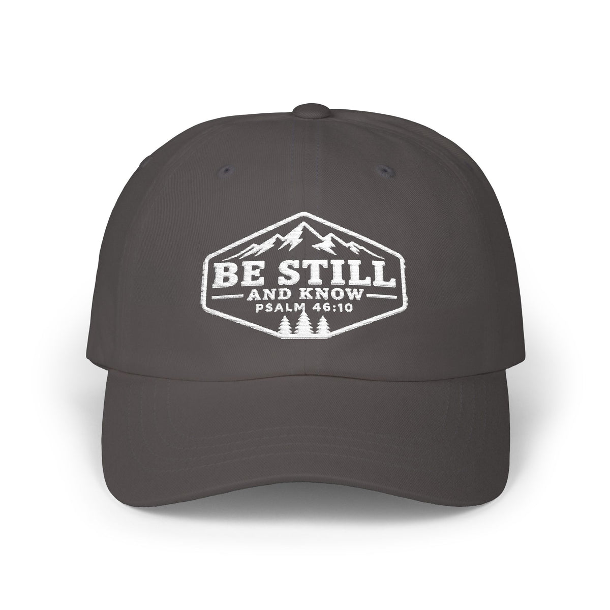 A dark gray baseball cap with a white graphic on the front featuring a mountain logo and the text 'BE STILL AND KNOW PSALM 46:10'.