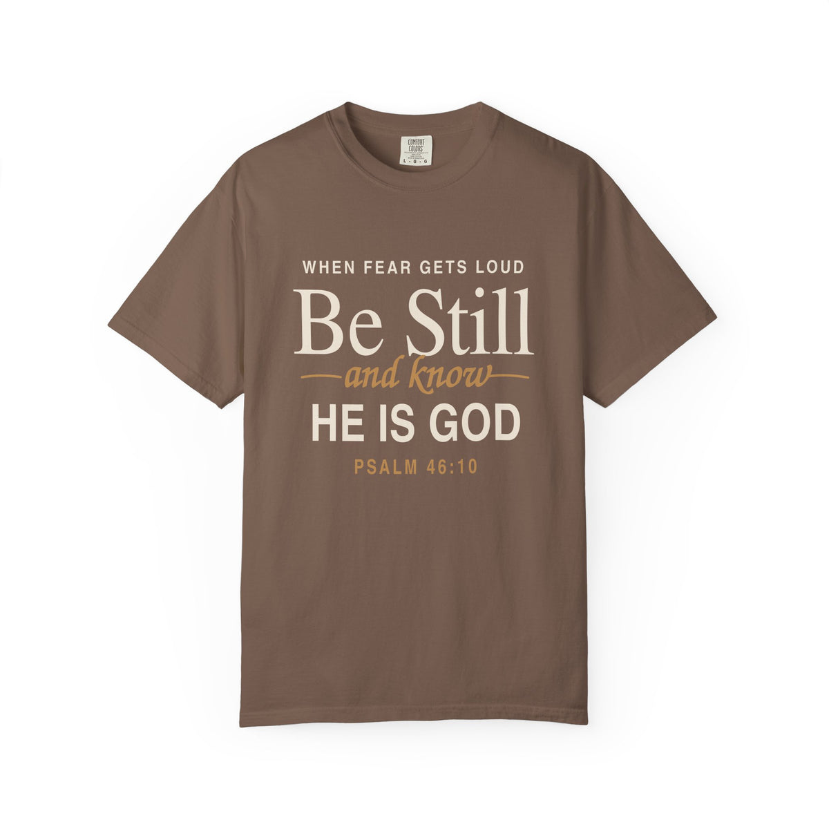 Brown Christian T-shirt reading “When Fear Gets Loud, Be Still and Know He Is God” with Psalm 46:10 on a plain white background.