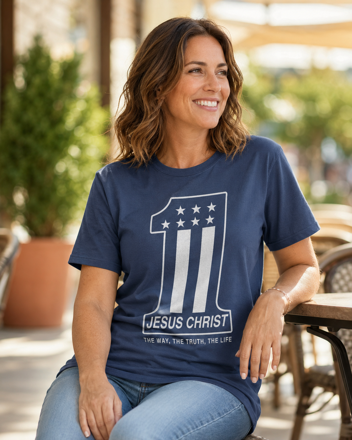 A woman smiling while wearing a navy blue graphic t-shirt with a white design featuring the number 1, stars, and the text 'JESUS CHRIST THE WAY, THE TRUTH, THE LIFE'.