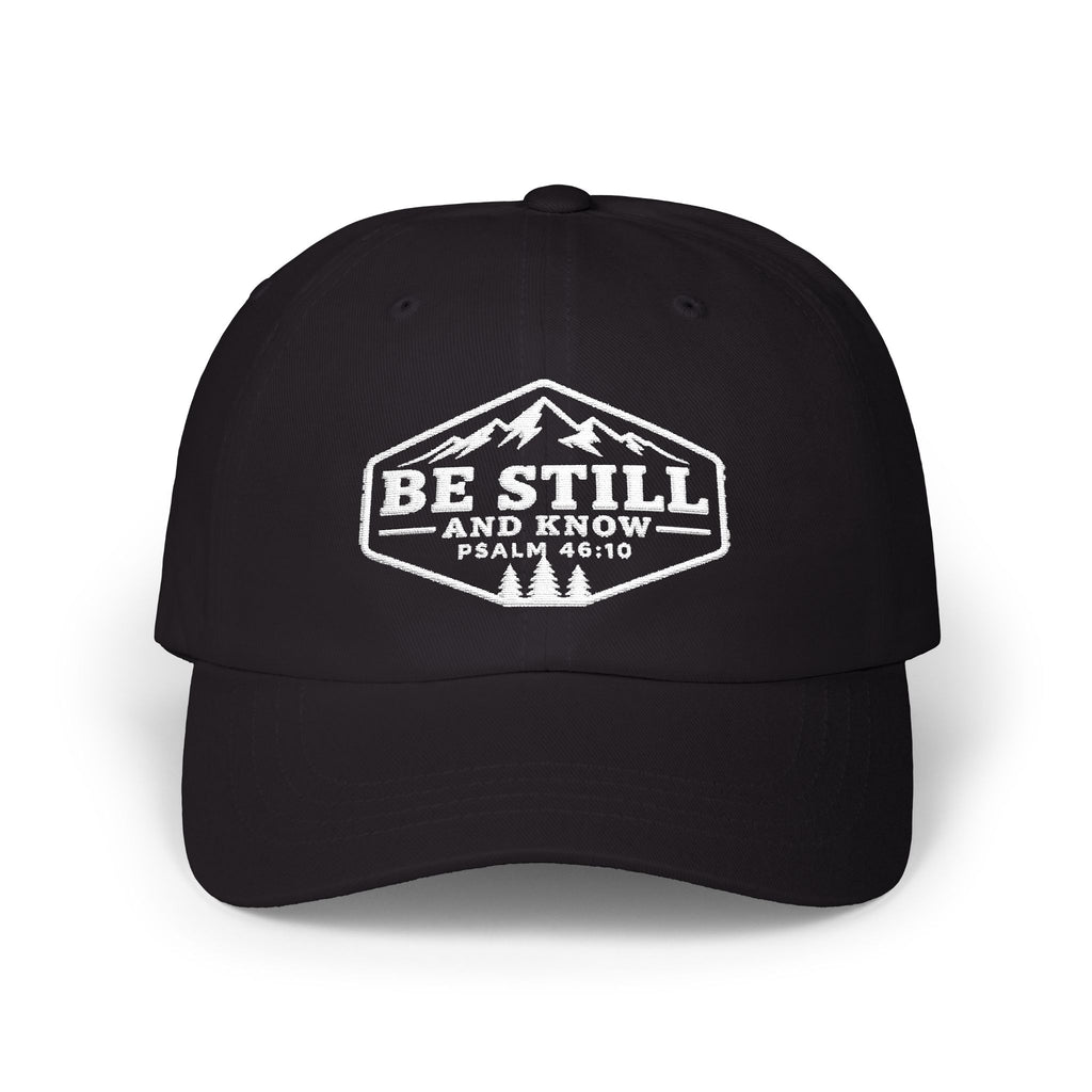 A black baseball cap with a white embroidered graphic on the front featuring a mountain and pine tree design, with the text 'BE STILL AND KNOW PSALM 46:10'.