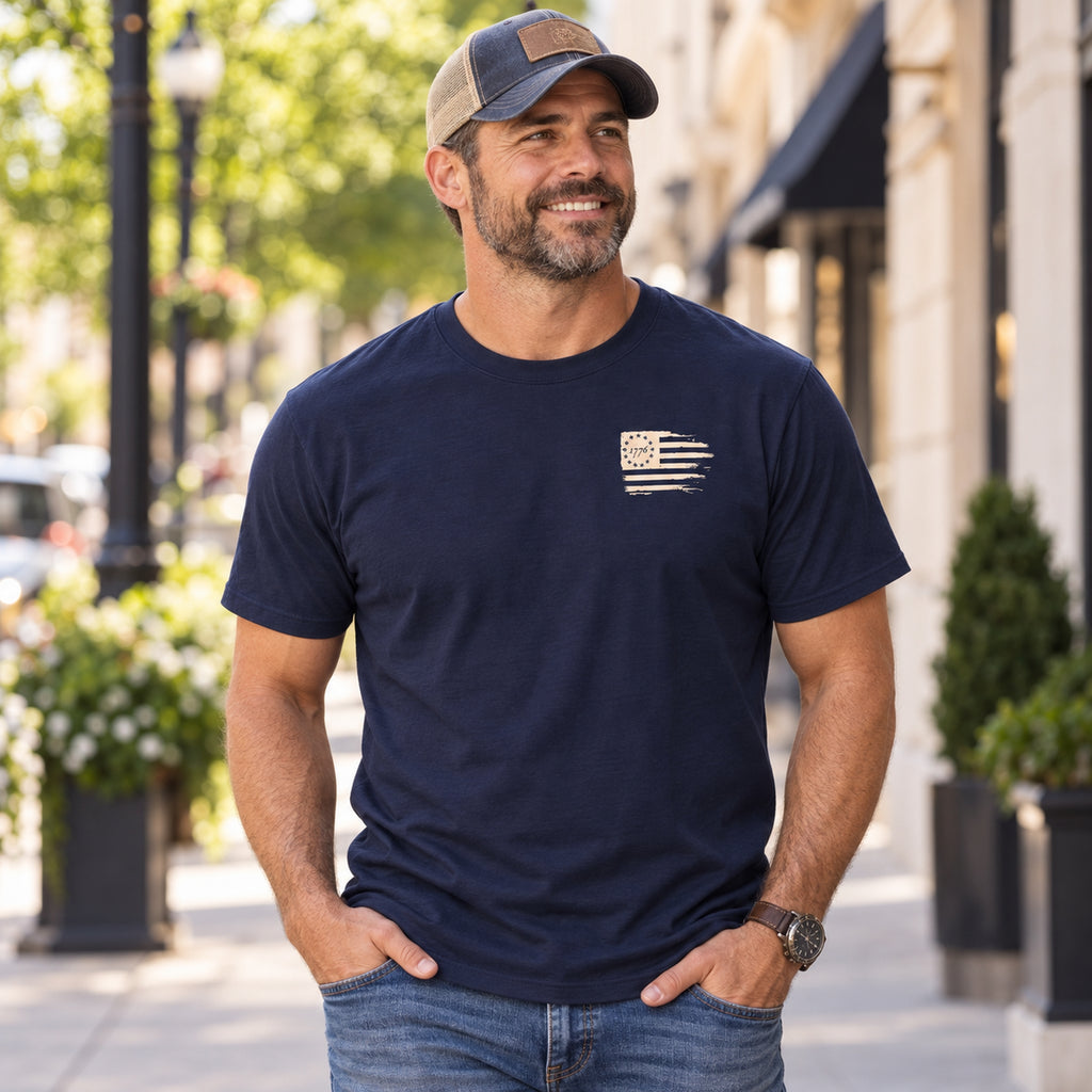 Man wearing navy Christian crew-neck T-shirt with small cream distressed 1776 American flag design on left chest.