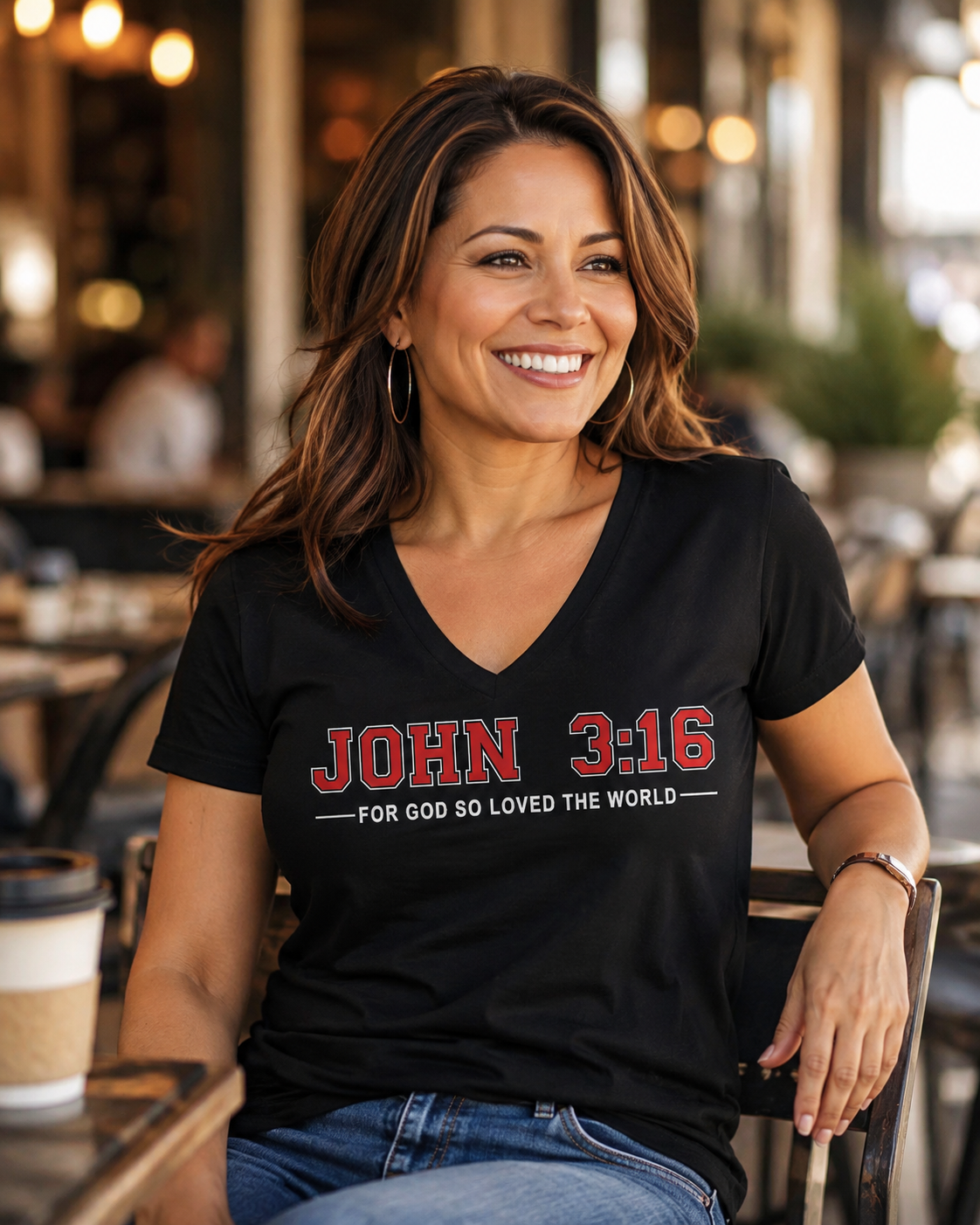 Woman wearing a black John 3:16 Christian V-neck T-shirt with “For God So Loved the World” design in a casual café setting.